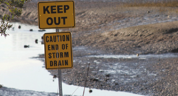 At the terminus of a storm drain in Newport Bay in Orange County, a pair of yellow signs reads: "Keep out" and "Caution -- End of Storm Drain."