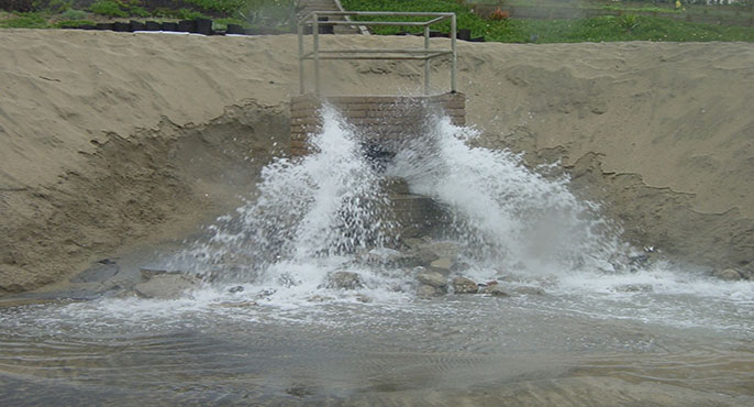 Water sprays out of a storm drain onto a beach during wet weather.