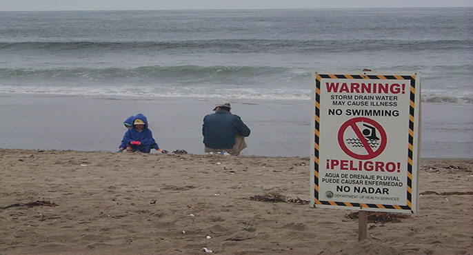 A warning sign on the beach reads: “Warning. Bacteria levels exceed heath standards ocean water contact may cause illness. No Swimming.”