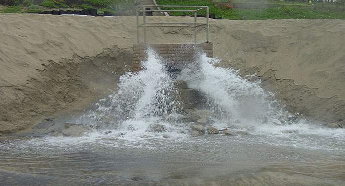 Water sprays out of a storm drain onto a beach during wet weather. 