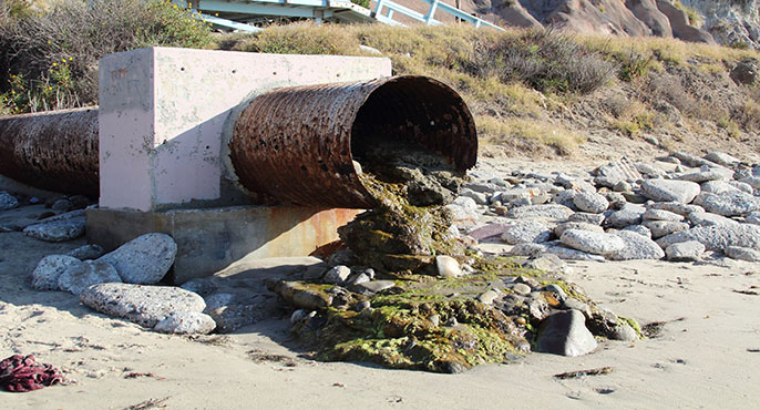 A large storm drain pipe that terminates at a Southern California beach deposits a trickle of dry-weather runoff onto the sand.